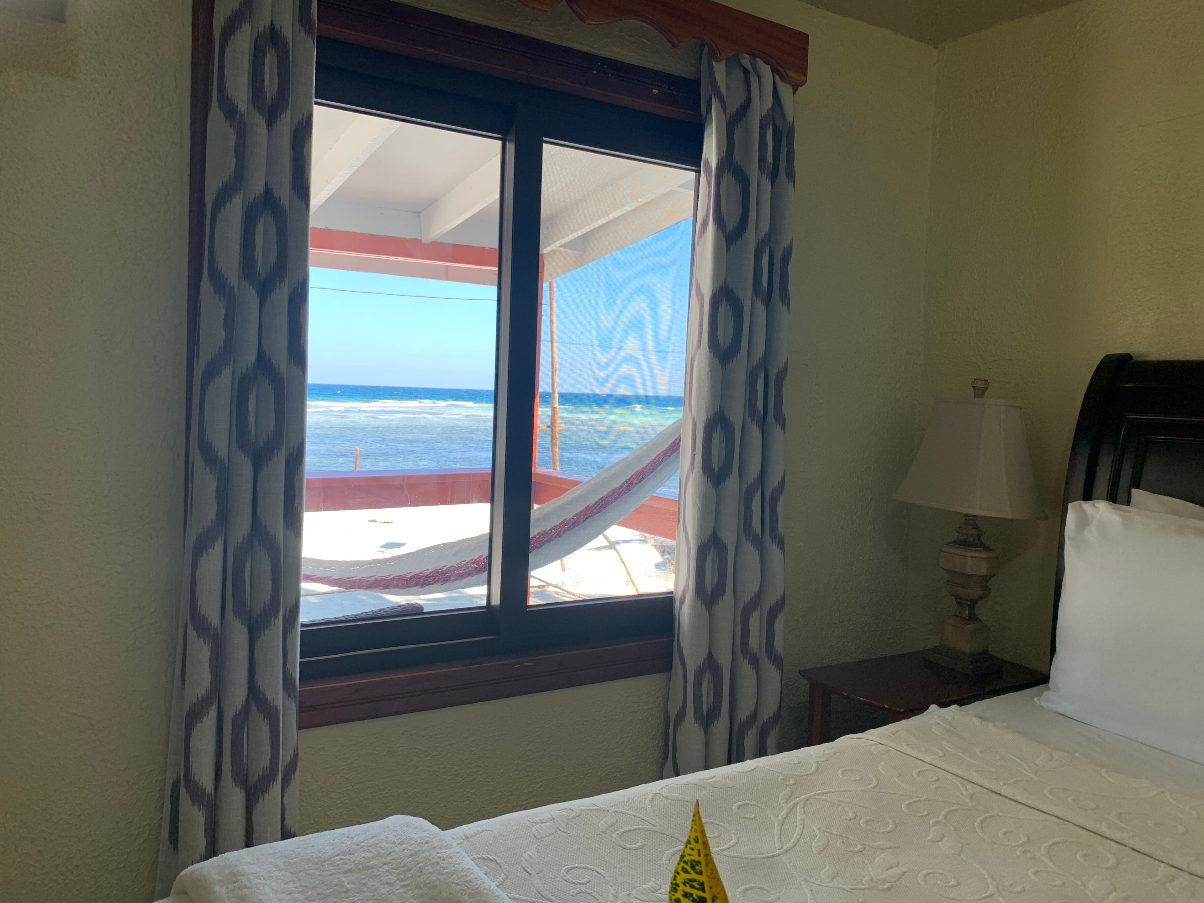 A cozy bedroom with a window view of the ocean and a hammock outside.