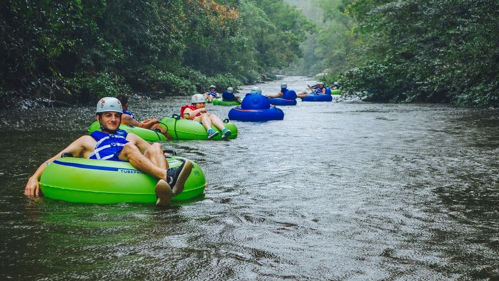 Several smiling people tubing down a river through the jungle.