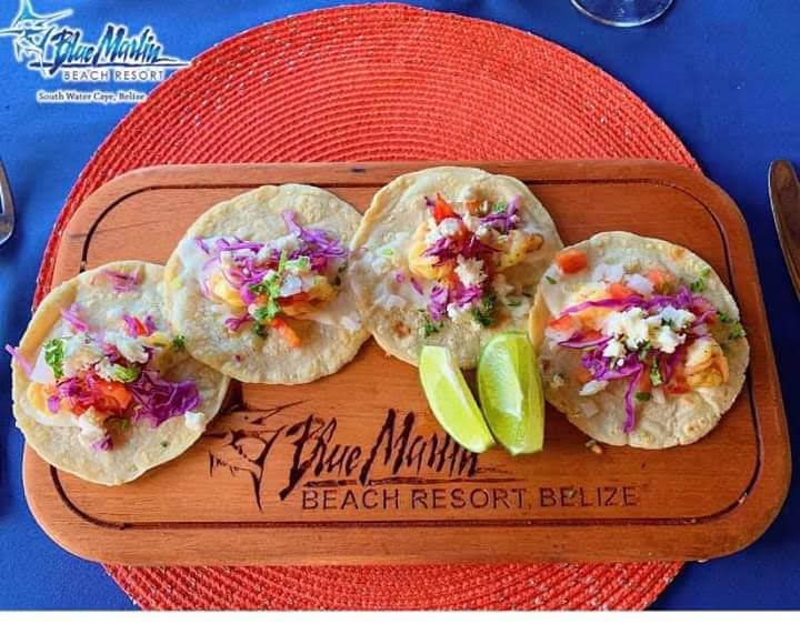 A wood board with Blue Marlin Beach Resort Belize burned into the board, and several freshly made corn tortillas and fish tacos