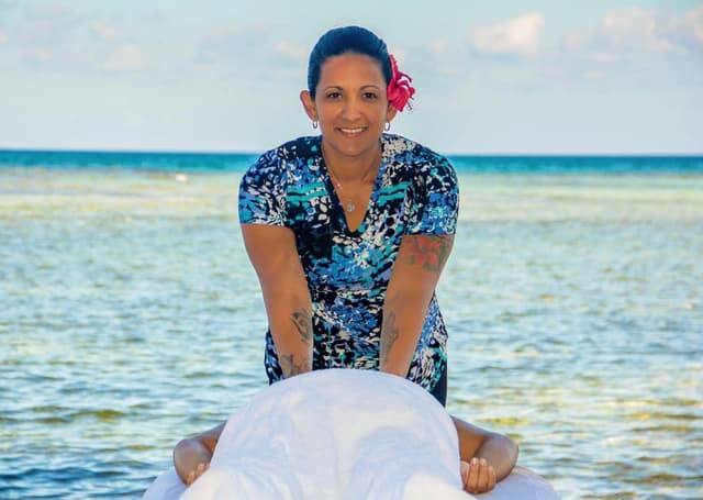 A smiling woman giving someone a massage on the beach