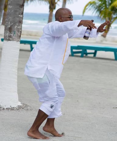 A man dancing and laughing on a sandy beach with a beer in his hand