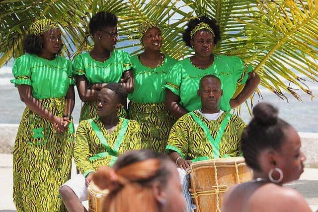 A group of women in colorful green, yellow and black dressing smiling and posing for a picture